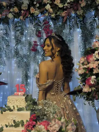 Debutante de vestido dourado diante do bolo de 15 anos